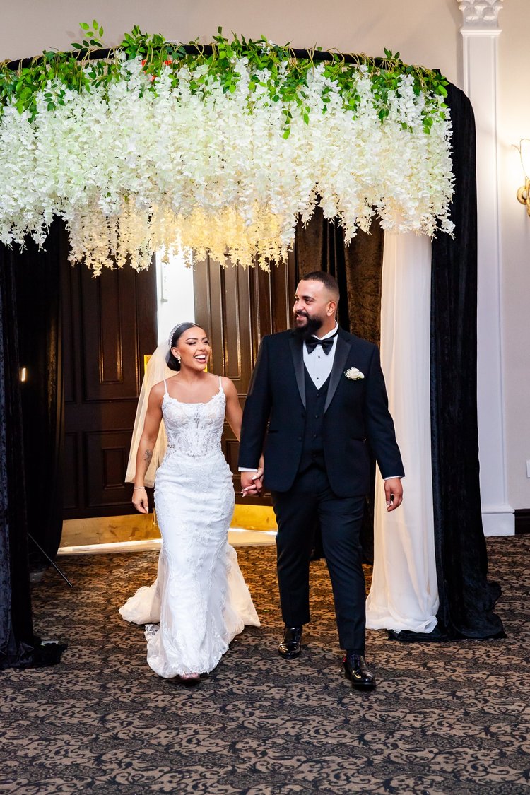 Bride and groom walking beneath a floral wedding arch