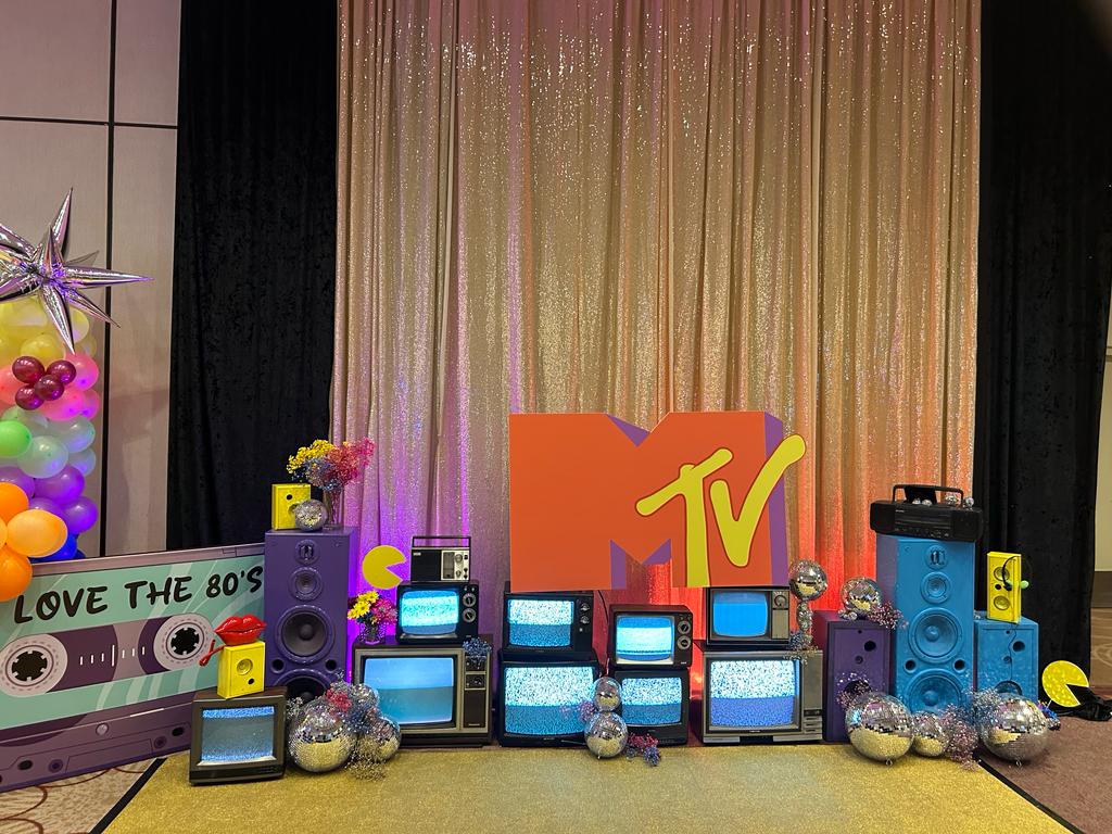 Custom MTV-inspired event environment by Alexandria Design House with illuminated vintage televisions, architectural speakers and an oversized MTV installation